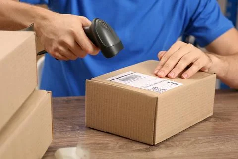 Post office worker with scanner reading parcel barcode at counter, closeup Stock Photos