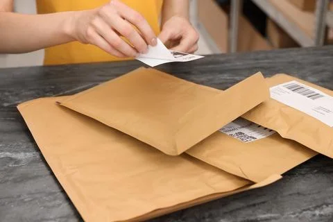 Post office worker sticking barcode on parcel at counter indoors, closeup Photos