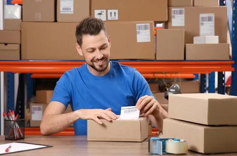 Post office worker sticking barcode on parcel at counter indoors Stock Photos