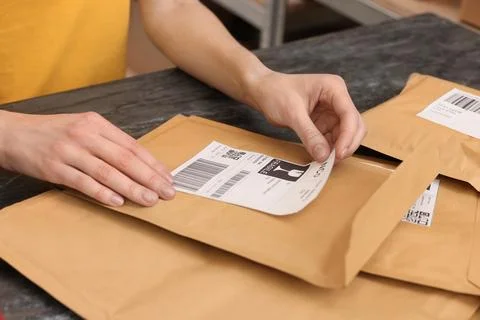 Post office worker sticking barcode on parcel at counter indoors, closeup Foto stock