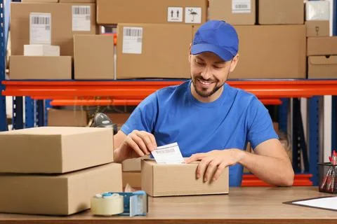 Post office worker sticking barcode on parcel at counter indoors Stock Photos