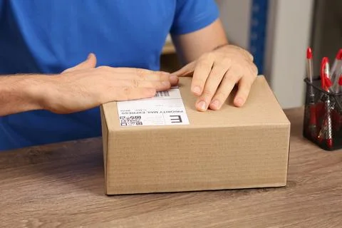 Post office worker sticking barcode on parcel at counter indoors, closeup Photos