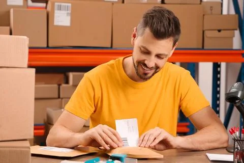 Post office worker sticking barcode on parcel at counter indoors Photos