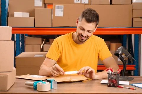 Post office worker sticking barcode on parcel at counter indoors Stock Photos