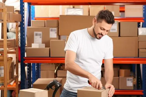 Post office worker with utility knife opening parcel indoors Foto stock