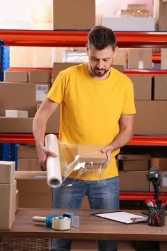Post office worker wrapping parcel in stretch film at counter indoors Photos