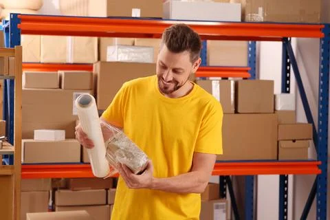 Post office worker wrapping parcel in stretch film indoors Photos