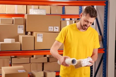 Post office worker wrapping parcel in stretch film indoors Foto stock