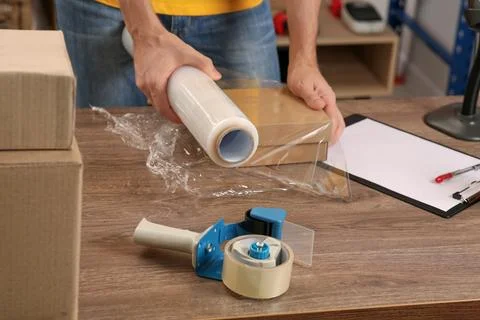 Post office worker wrapping parcel in stretch film at counter indoors, closeu Stock Photos
