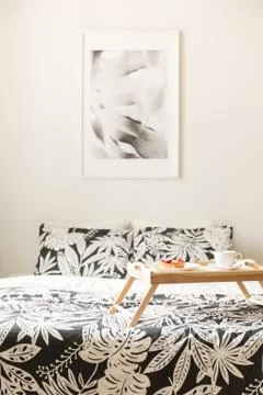 Poster above bed with patterned sheets and wooden tray in white hotel bedroom Stock-Fotos