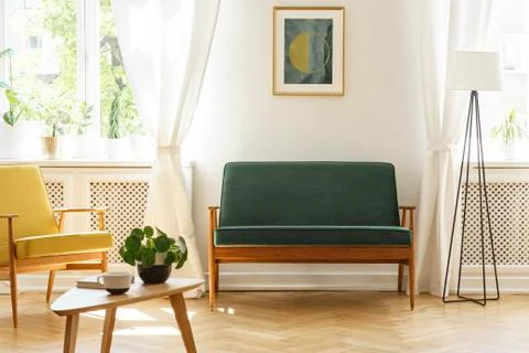 Poster above green bench between lamp and yellow armchair in vintage living r Stock Photos