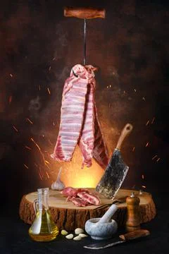 Poster with raw lamb ribs on hook over wooden stumb Stock Photos