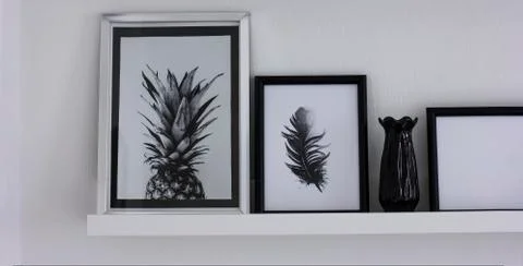 Posters with pineapple and feather on the shelf, modern interior in black and Stock Photos