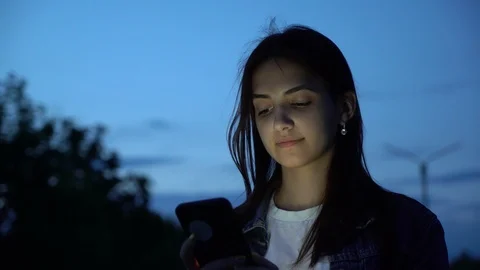 Postive young girl using smartphone on the low-light street in the park in the Video stock 109652873