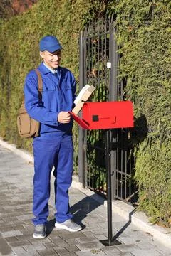 Postman putting parcel into mail box outdoors Stock Photos