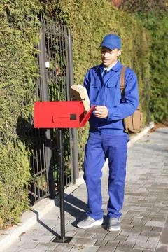 Postman putting parcel into mail box outdoors 库存照片