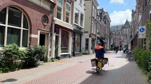 PostNL postman on bicycle with the orange saddle bags with logo cycling and Stock Footage 280230783