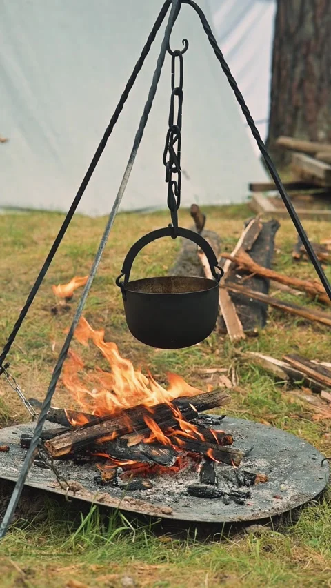 A pot hangs from a tripod over an open fire, cooking food in a historical Stockbeeldmateriaal 345036553
