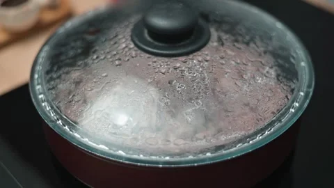 Pot with a lid sits on a stove, displaying steam and condensation on the glass 스톡 동영상 337112200