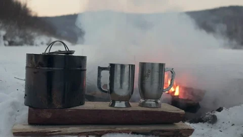 A pot with mugs stand on a log against the background of a fire. Stock Footage 83538689