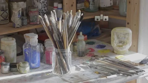 Pot of paintbrushes sitting on a table surrounded by paint Vídeos de archivo 147198458