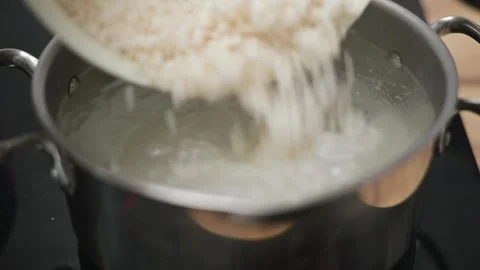 A pot is placed on a burner as water is poured in, followed by rinsed rice being Stock Footage 338298526
