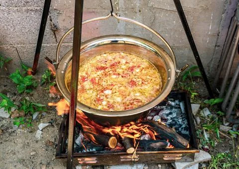 Pot with vegetables cauldron over open fire, preparing stew soup on wood gril Stock Photos