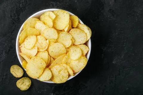 Potato chips. Crispy potato chips in bowl on a dark stone concrete background Stock Photos