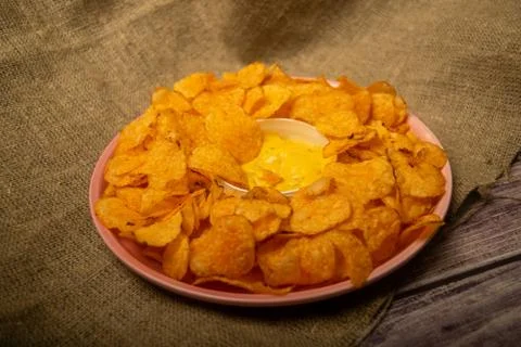 Potato chips on a round platter and a saucepan with cheese sauce. Close up. Stock Photos