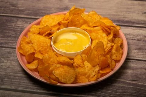 Potato chips on a round platter and a saucepan with cheese sauce. Close up. Stock Photos