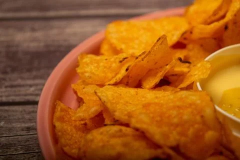 Potato chips on a round platter and a saucepan with cheese sauce. Close up. Stock Photos
