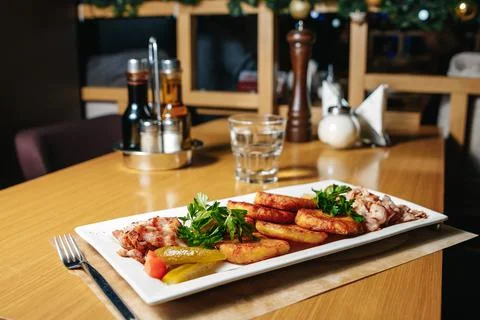 Potato pancakes with bacon on a white rectangular plate on a table in a resta Stock Photos
