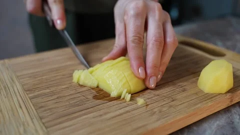Potatoes are being sliced on a cutting board. Stockbeeldmateriaal 303573754