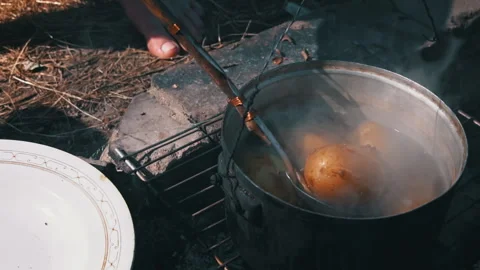 Potatoes are Cooked in a Large Cauldron Over an Open Fire During the Day Stock Footage 250240882