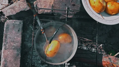 Potatoes are Cooked in a Large Cauldron Over an Open Fire During the Day Stock Footage 252807757