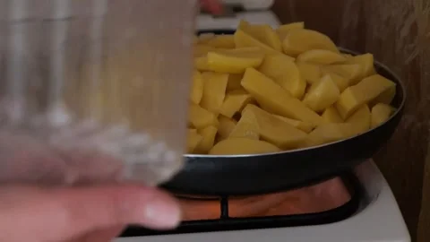Potatoes are poured from plastic container into frying pan on a gas stove Stock-Footage 306410148