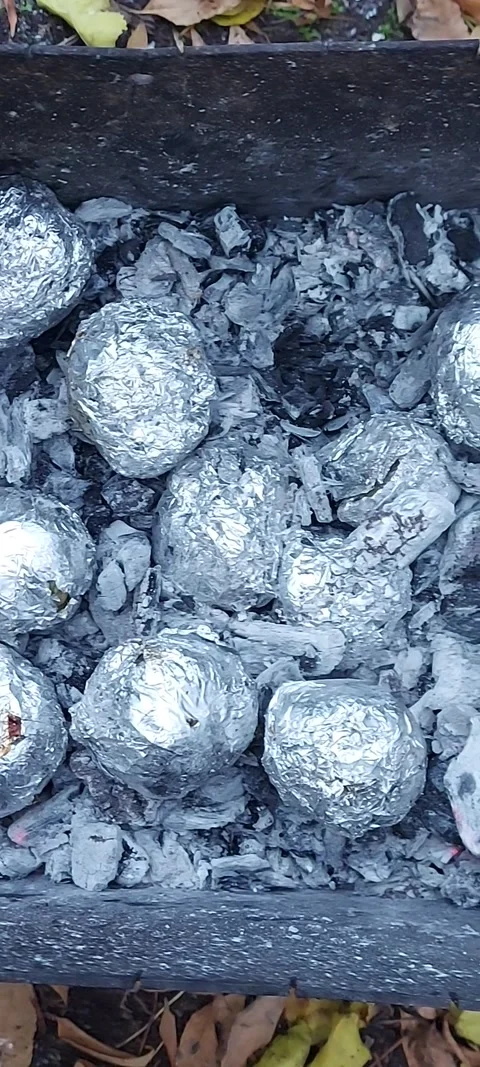Potatoes wrapped in foil are baked on charcoal. Street hearty food Stock Footage 320193333
