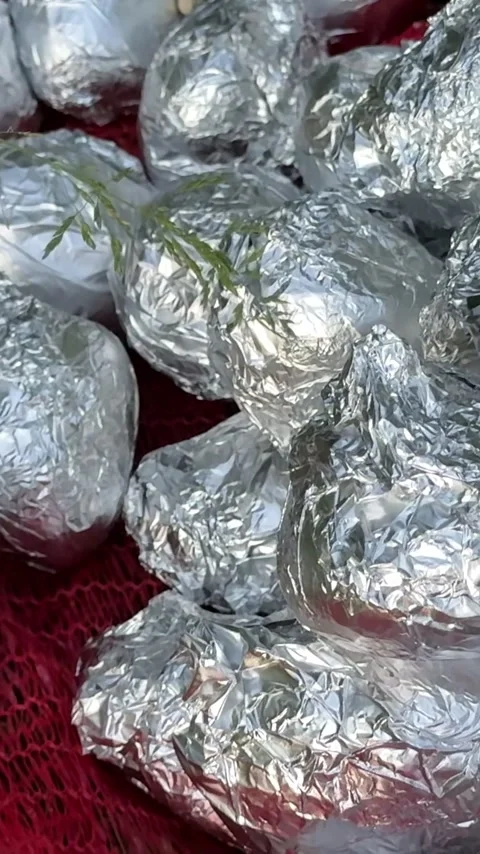 Potatoes wrapped in foil resting on grass on red mesh prepared for baking over Vídeos de archivo 345726531