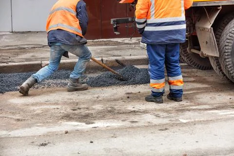 Pothole repair of the road. A team of workers patches holes in the old paveme Stock Photos
