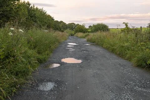 Potholes on rough compacted hardcore road or countryside farm track Stock Photos