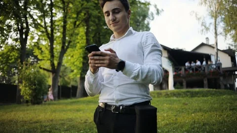 Potrait attractive young man use phone smile walk in park forest internet sunset Stock Footage 95447060
