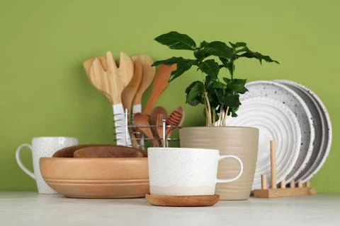 Potted plant and set of kitchenware on white table near green wall. Modern in Stock Photos