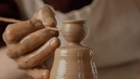 Potter adds unique lines to vase on potter's wheel. Close-up of potter's hands. Video stock 245156471