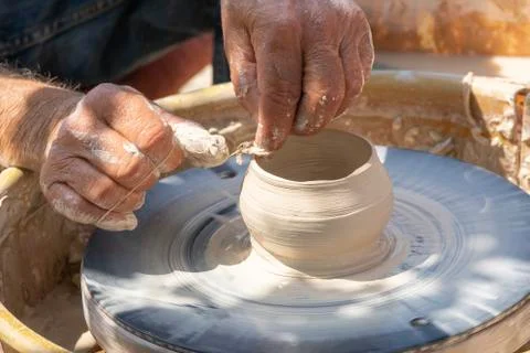 Potter cuts the edges of pottery with thread on spinning wheel. Outdoor Stock Photos