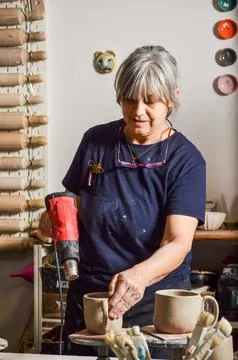 Potter using heat gun drying clay mugs in workshop Stock Photos