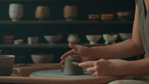 Potter using scraping tool on clay cup on pottery wheel in studio Stock Footage 275086219