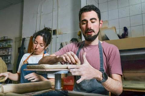Potter using sponge explaining clay work to female apprentice in workshop Stock Photos