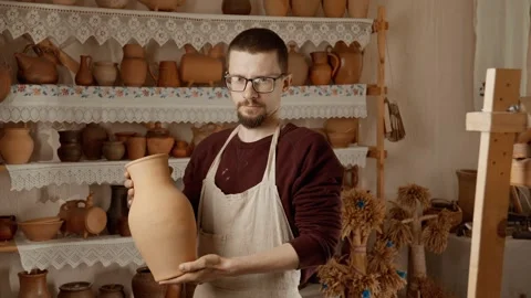 Potter with vase in hands looking at camera. Portrait of young craftsman Stock Footage 246179446