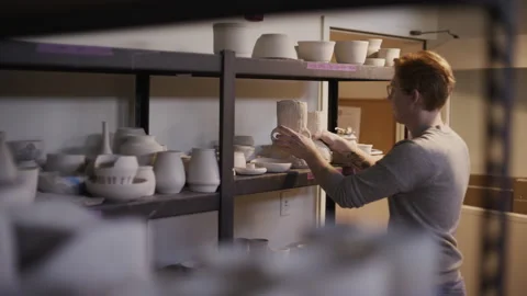 Potter working in studio putting ceramics on shelf Stock Footage 235466875