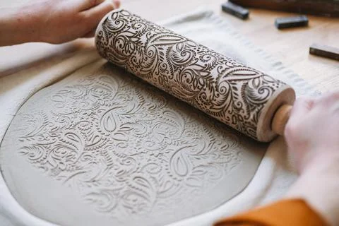 Potter's hands embossing pattern on clay plate with rolling pin Stock Photos